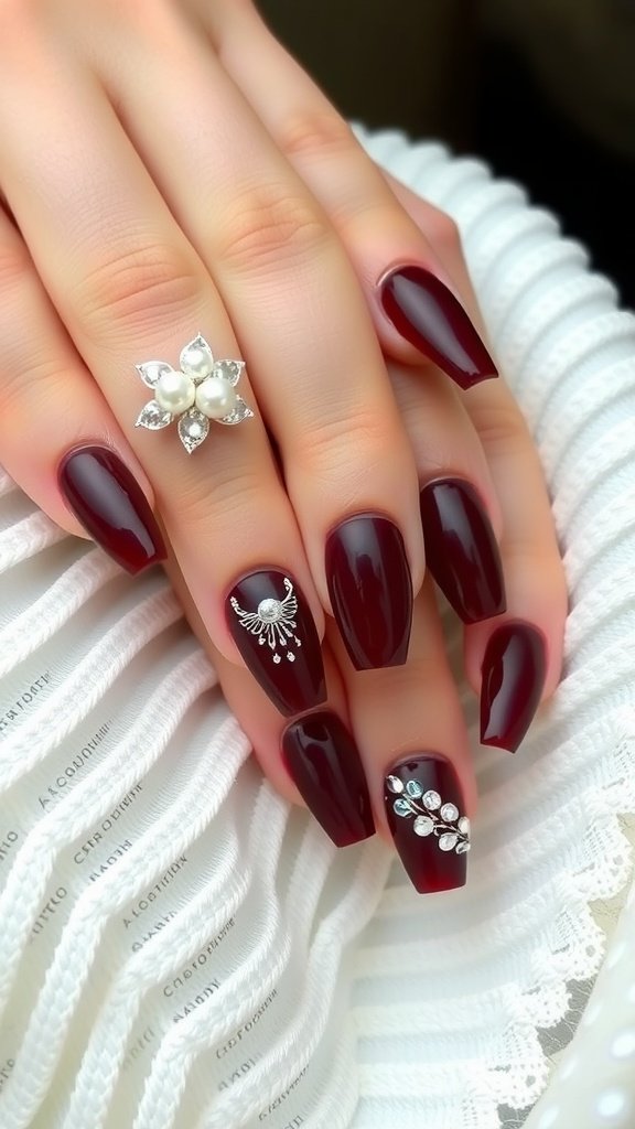 A close-up of cherry wine nails with pearl and jewel accents.