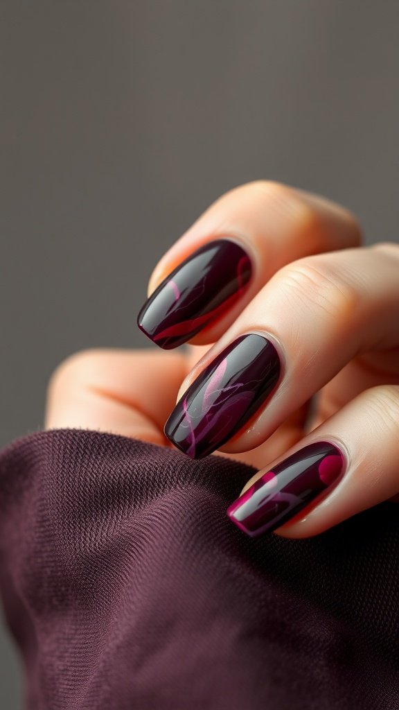 Nails with a cherry wine marble effect against a soft fabric background.